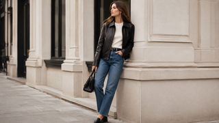 Woman styling a classic black leather jacket with a cream knit top, straight-leg jeans, and loafers on a city street