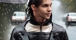 Man wearing a leather jacket in the rain under an umbrella.