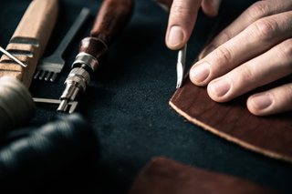 Hands crafting leather with precision tools on dark fabric surface