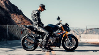 Man in biker leather jacket sitting on a motorcycle on mountain road