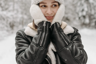 Woman in cozy shearling-lined leather jacket in snowy winter forest.