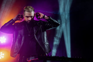 Stylish man in biker leather jacket DJing under vibrant stage lights.