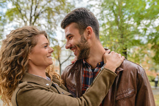 Smiling couple in brown leather jackets embracing outdoors in fall.